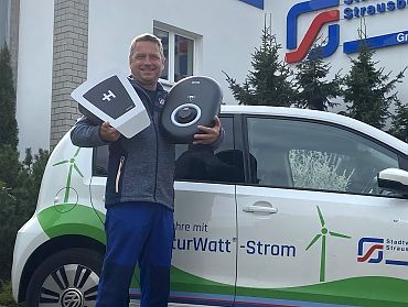 Ein Mitarbeiter steht vor einem Auto und hält technische Komponenten hoch